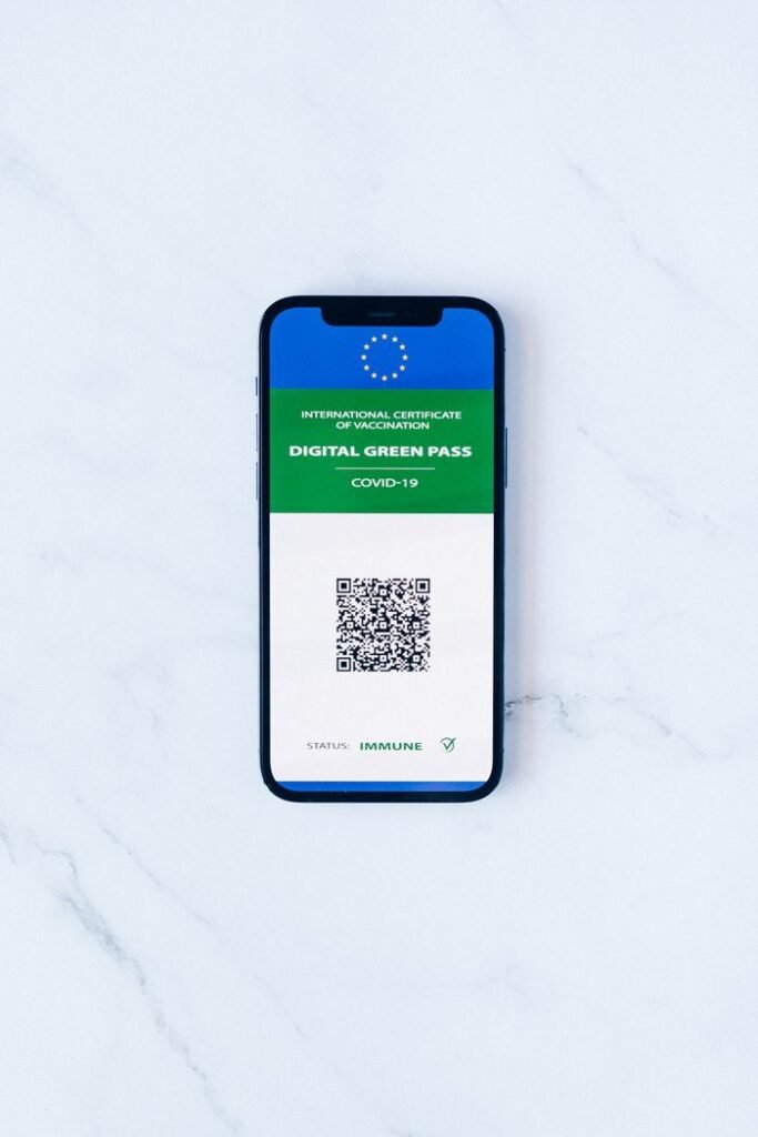 A smartphone displaying a digital green pass with QR code on marble surface.